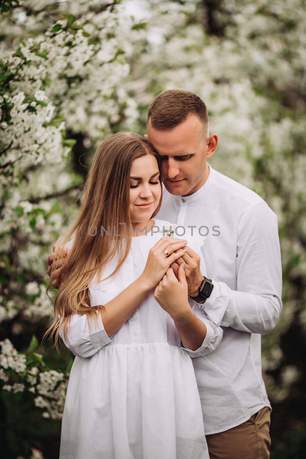 Happy family couple in love in a spring blooming apple orchard. Happy family enjoy each other while walking in the garden. The man holds the woman's hand. Family relationships by Dmitrytph