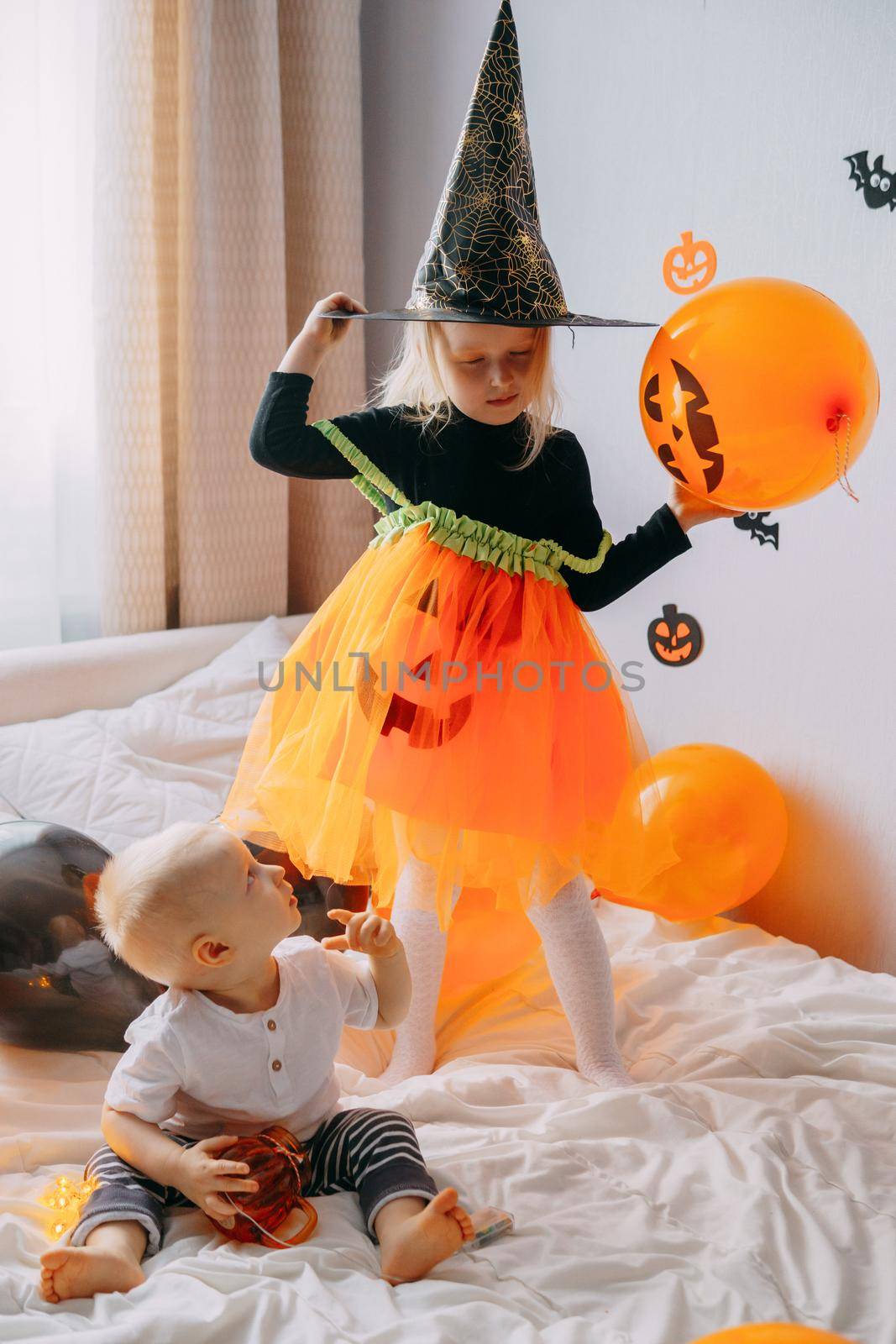 Children's Halloween - a boy and a girl in carnival costumes with orange and black balloons at home. Ready to celebrate Halloween by Annu1tochka