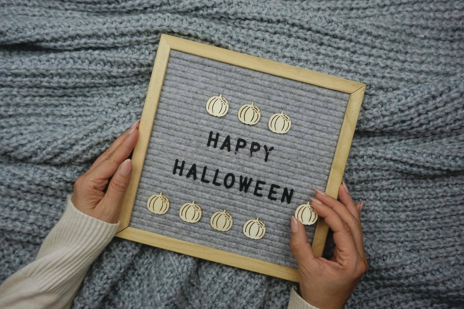 Women's hands hold a board with the text - Happy Halloween. Knitted background. Wooden pumpkin decor.