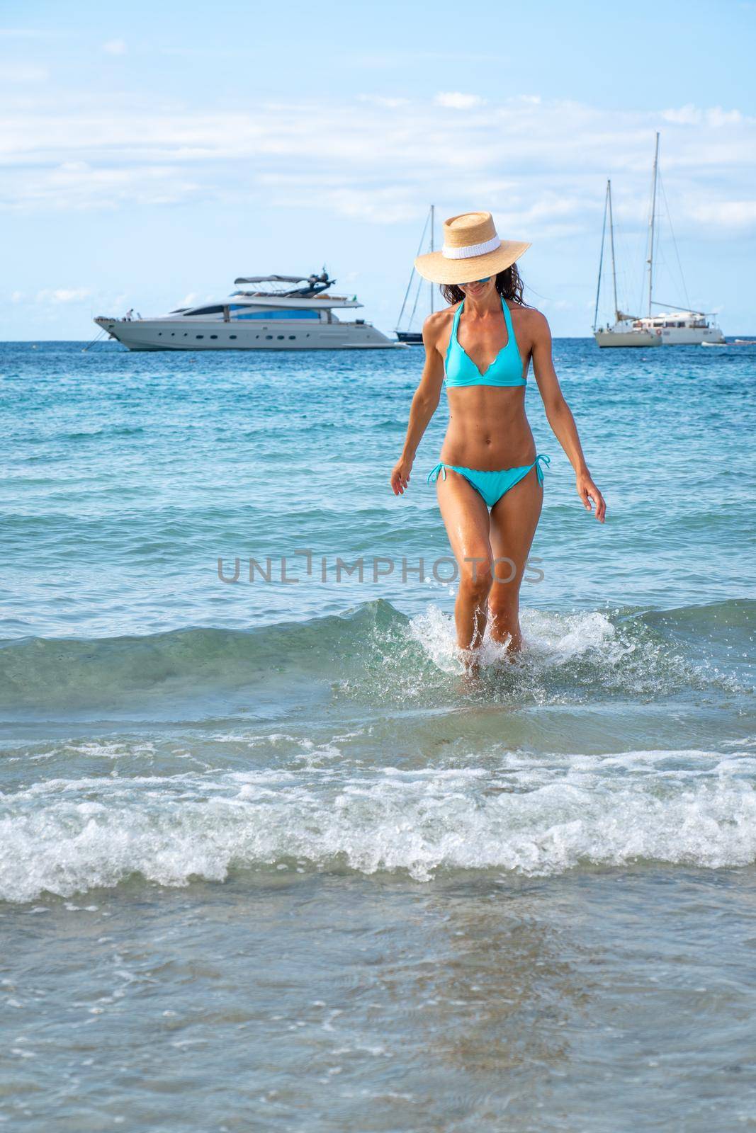 Woman with turquoise bikini and hat posing on a beach in Ibiza