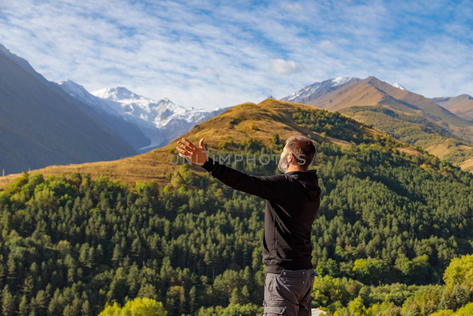 A man stands on top of a mountain with his arms outstretched