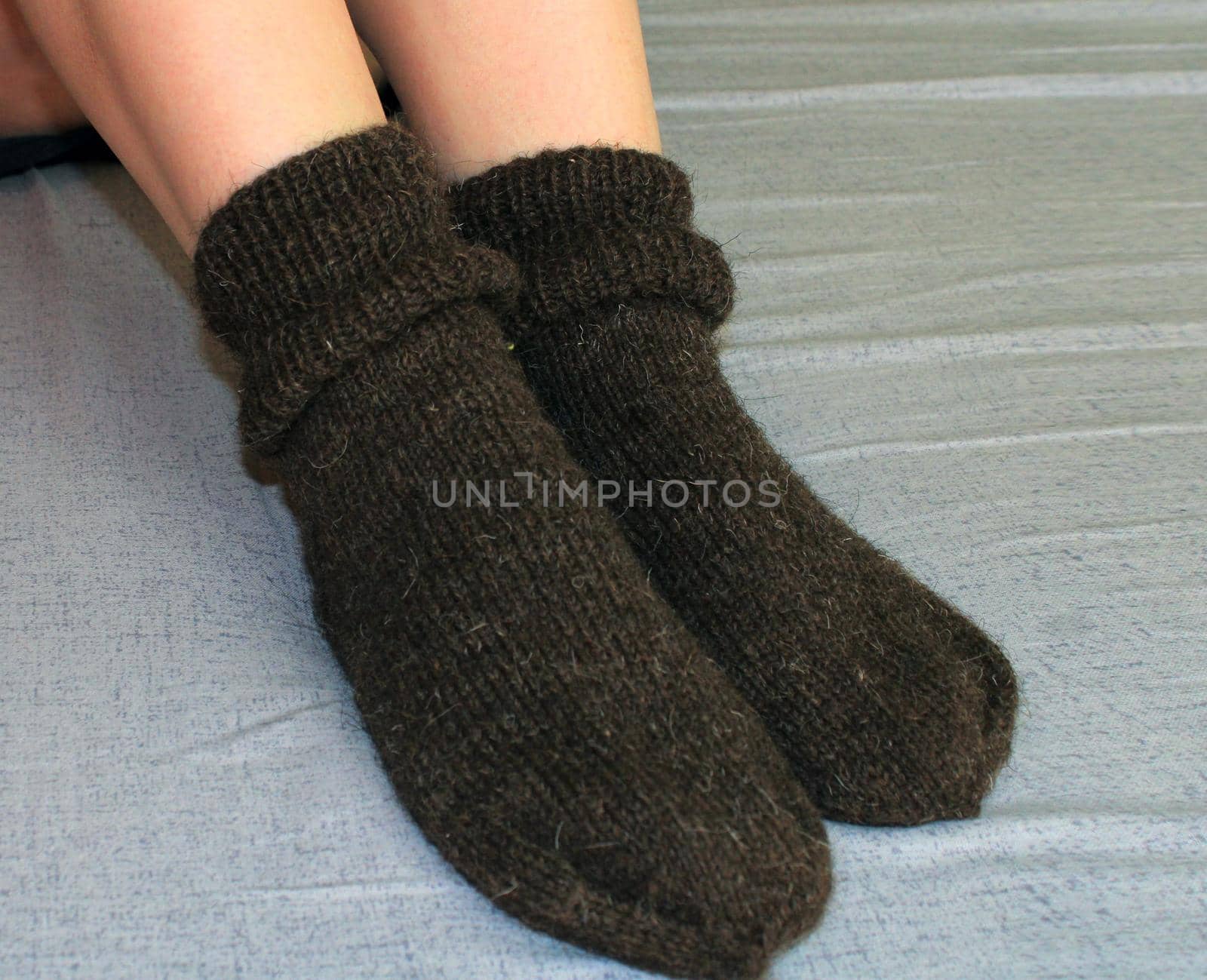 A young woman with slender legs sits on a bed at home in brown woolen socks. The concept of the world energy crisis.