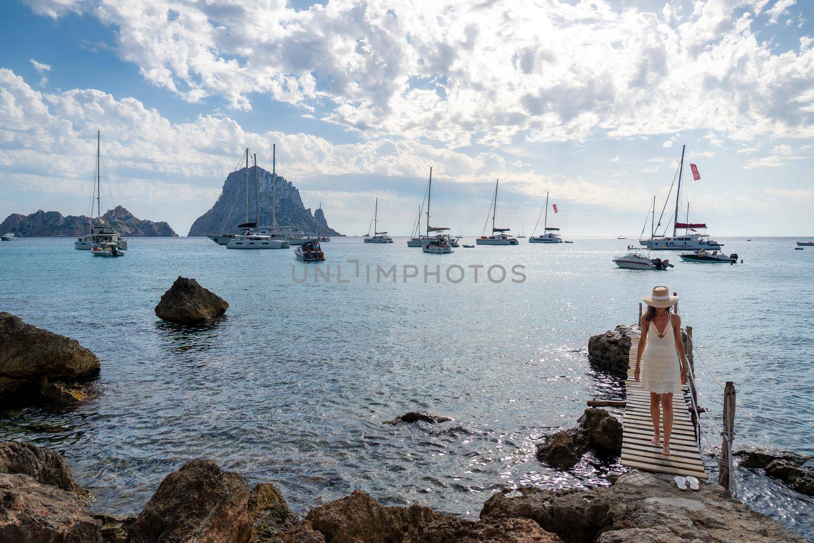 Brunette woman with hat and light beige dress on Ibiza pier