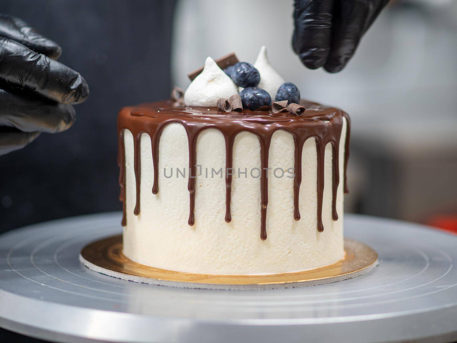 cake designer decorating a chocolate drip cake with mering and blueberries by verbano