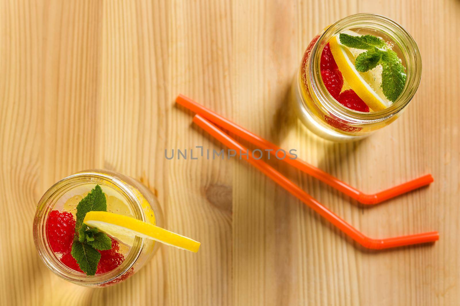 flat lay of two drink canes and two glass jars with refreshing cold lemonade water, lemon, red berries and mint on a wooden table lit by sunlight, Summer citrus refreshment background, Copy space