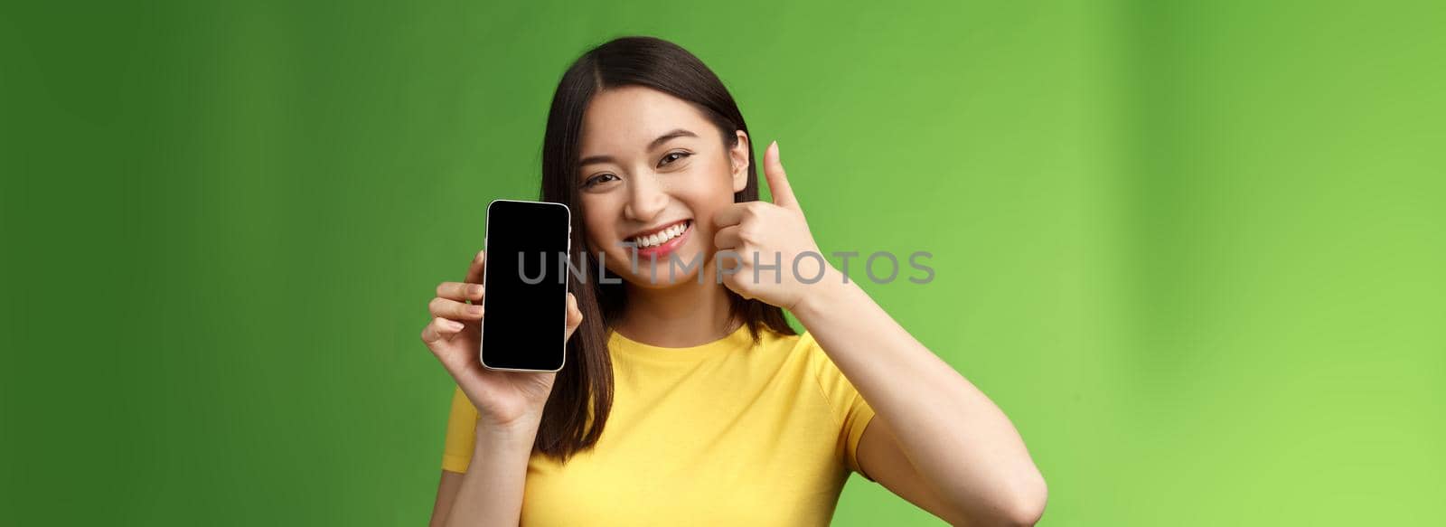 Close-up satisfied cute asian girl give positive feedback, thumb-up showing smartphone screen, introduce awesome new app, recommend good application, bragging beating score in game.