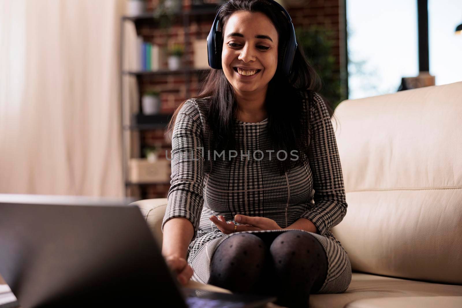 Indian person listening to podcast or webinar on headphones with laptop, working from home. Using online music or attending class lesson on network, browsing internet website.