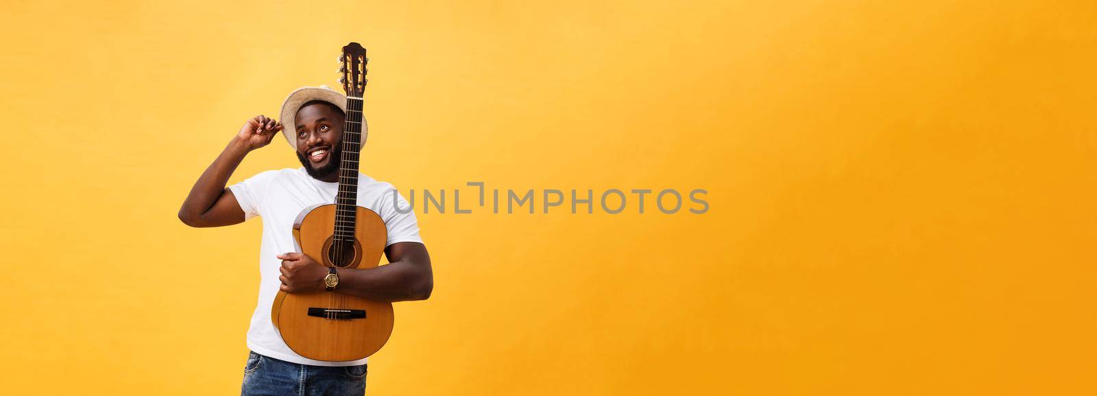 Muscular black man playing guitar, wearing jeans and white tank-top. Isolate over yellow background