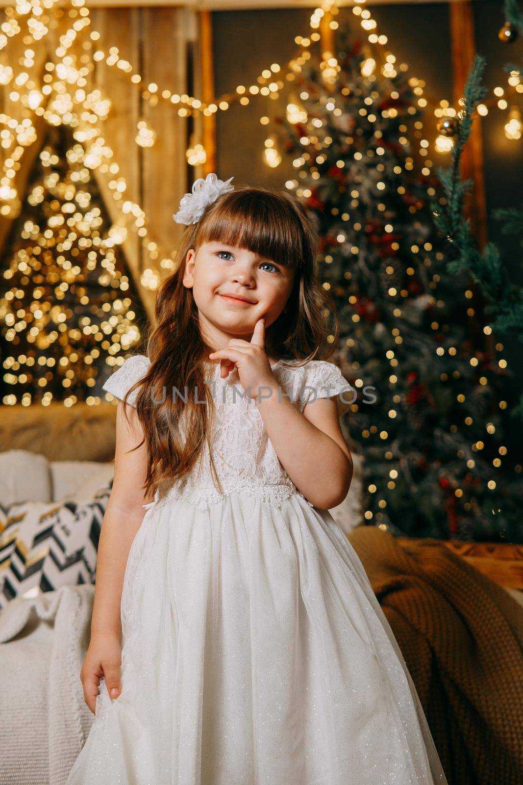 A girl in a festive light dress next to a Christmas tree, lights of garlands in the background. The concept of New Year holidays.