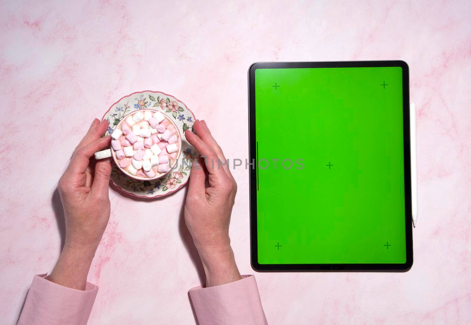 Young woman using tablet device with green screen and drinking hot cappuccino with marshmallow, chroma key. View over the shoulder. Close-up top view, High quality photo