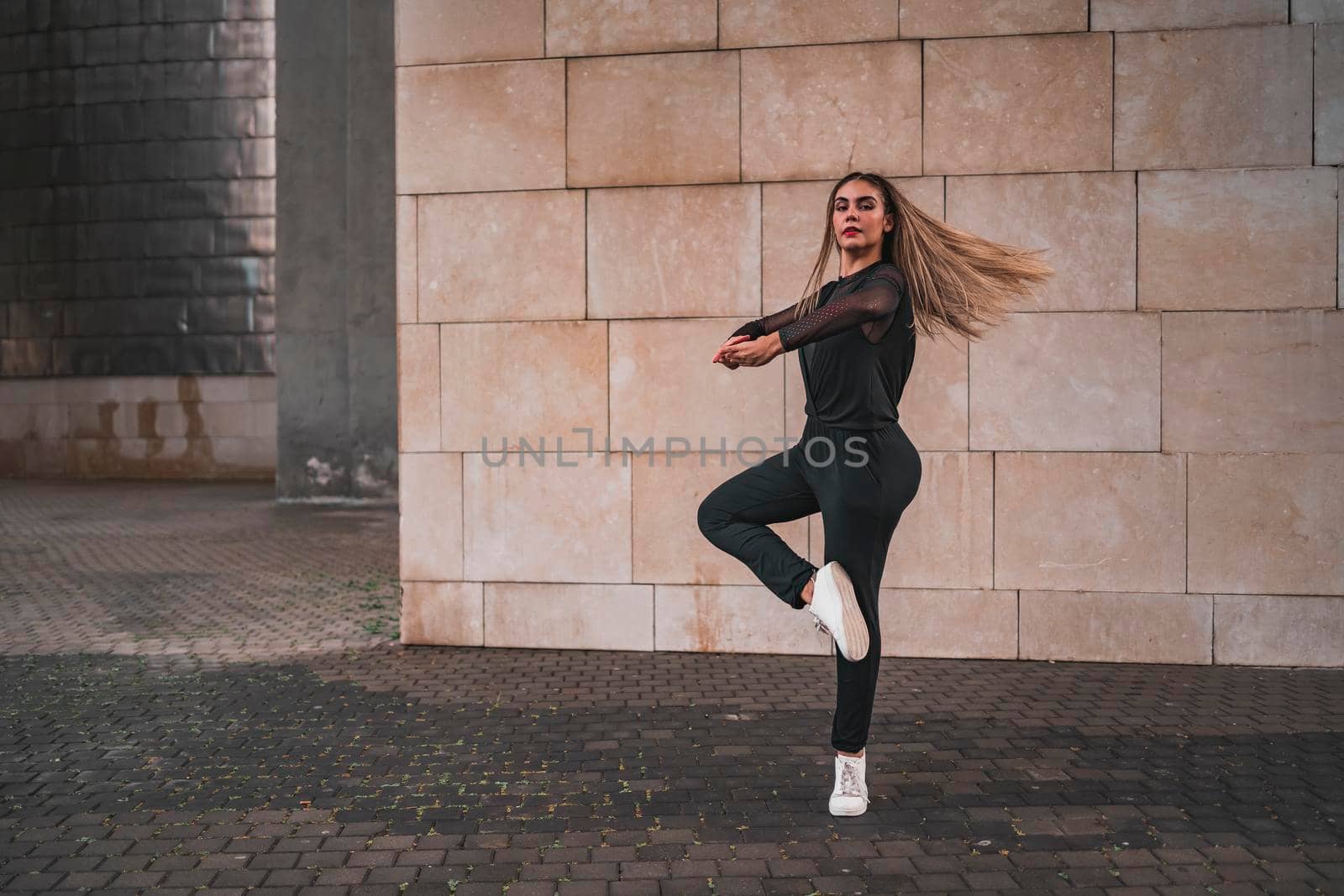A young ballerina in a black suit does ballet pirouettes on the street. by barcielaphoto