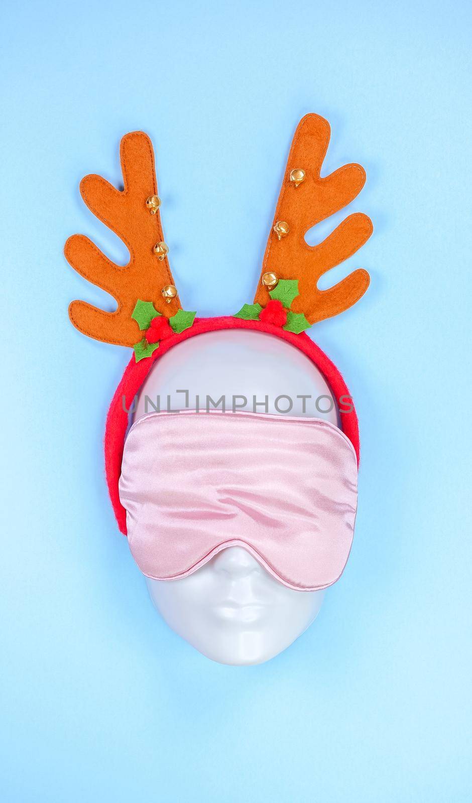 Pink sleeping eye mask on mannequin face with christmas horns on blue background, sleeping disorder. Holidays, Head accessory. Plastic face