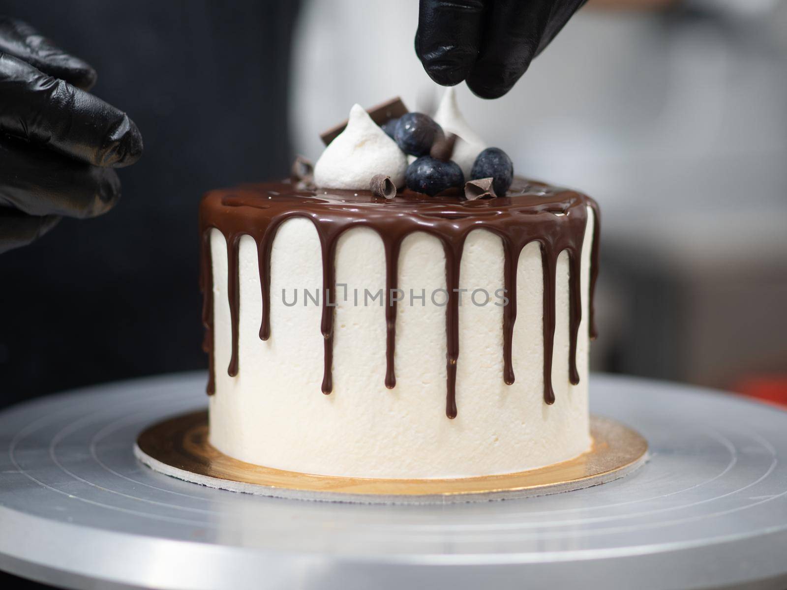 unrecognizable worker preparing a sweet dripping choco cake and berries