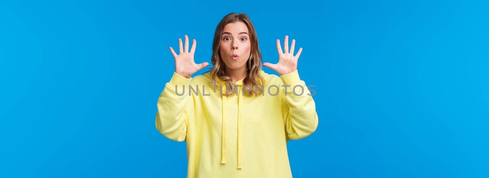 Imagine this. Excited and happy outgoing blond girl explain something and gesturing, holding hands near face, showing number ten, talking to camera passionatly describe plan, blue background.