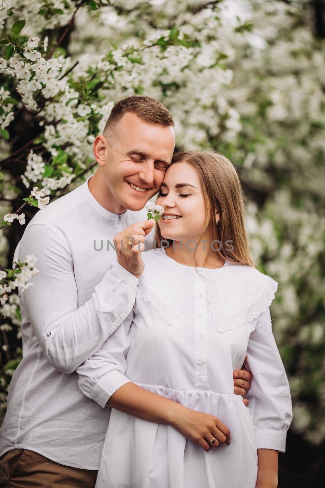 Happy family couple in love in a spring blooming apple orchard. Happy family enjoy each other while walking in the garden. The man holds the woman's hand. Family relationships by Dmitrytph