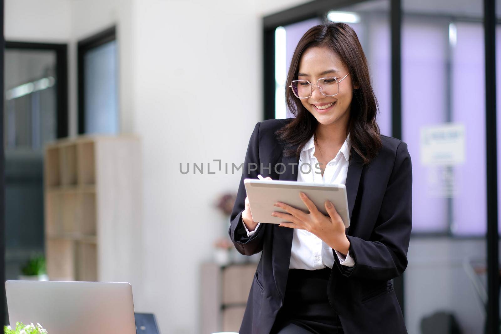 Beautiful businesswoman using stylus pen writing on tablet screen while standing in office room with copy space..