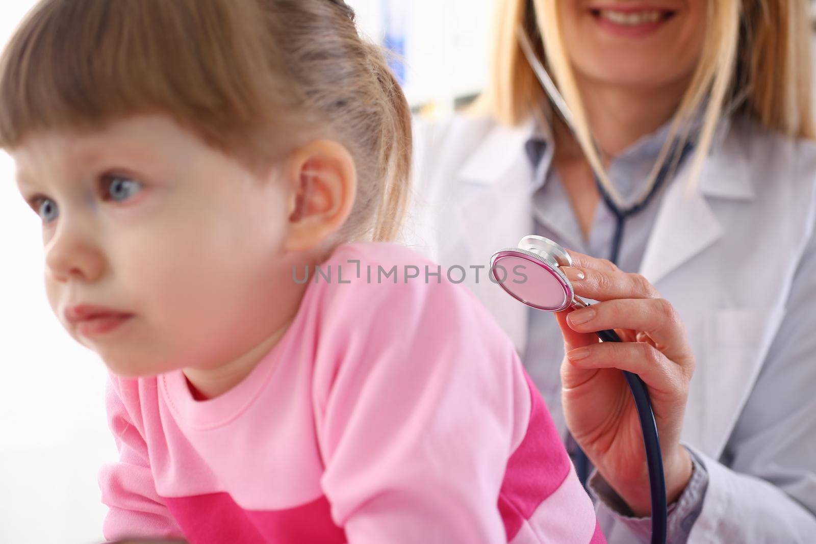 Pediatrician listens to lungs of small child girl with stethoscope. Children health insurance and examination of lungs and heart
