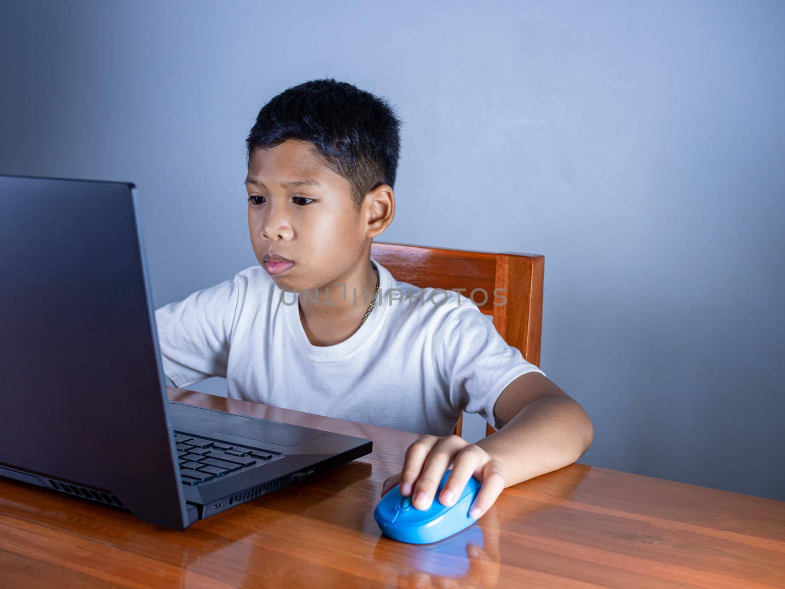 Close up The boy sits staring at the laptop and his hand is holding the mouse. educational concept, educational information search, copy space by Unimages2527