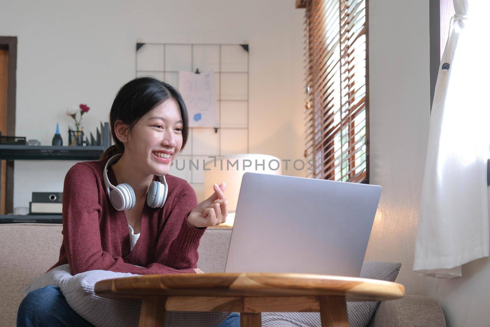 Attractive smiling young woman video call by laptop on sofa at home. lifestyle concept by wichayada