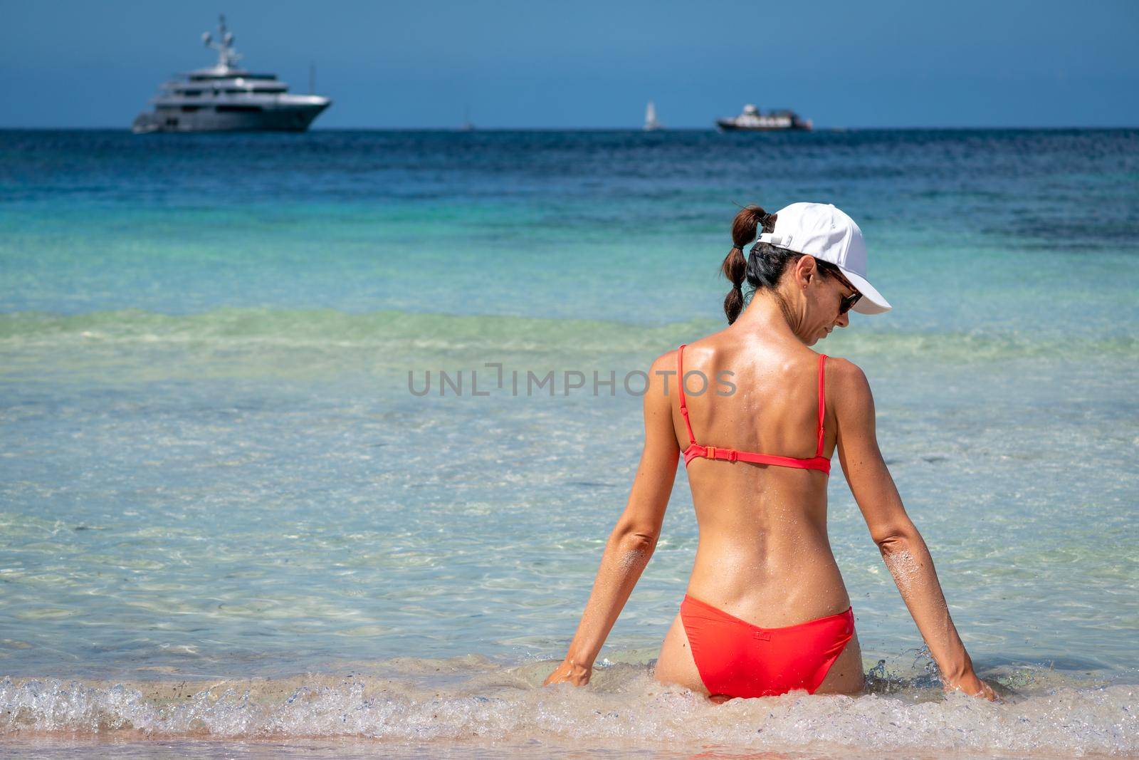 Brunette woman with coral bikini and cap posing on the beach