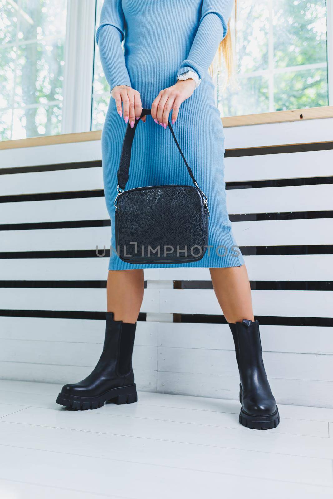 Fashionable leather boots on a woman's leg, close-up, fashionable. Leather bag in female hands.