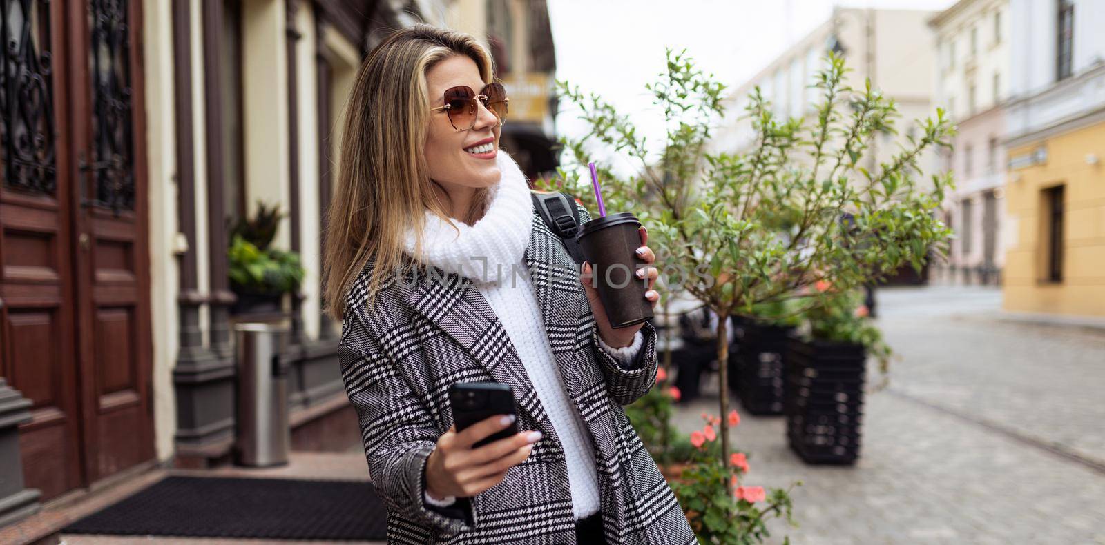 woman Tourist walks around the city sightseeing with a cup of coffee and a mobile phone.