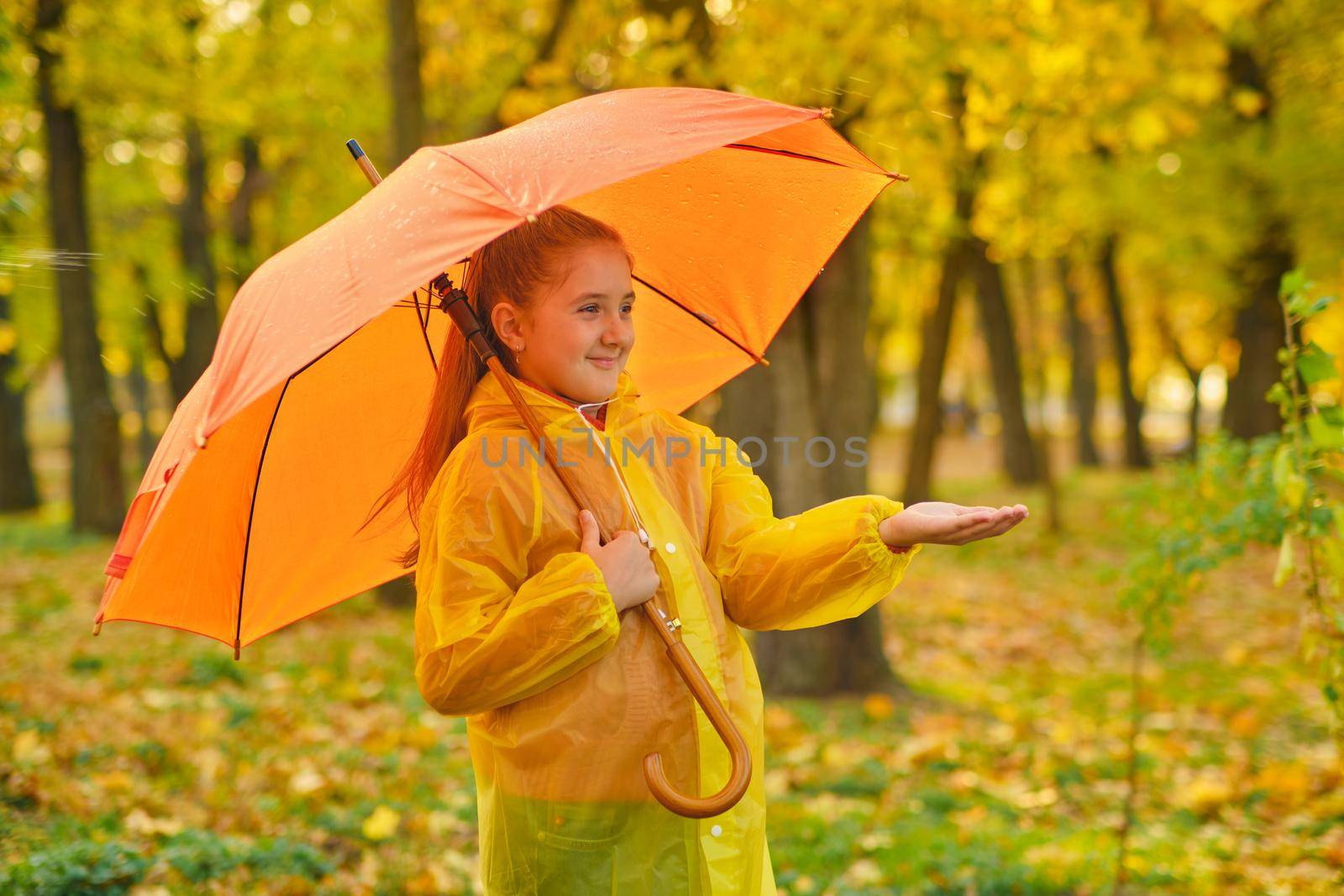 Happy child in the rain. Funny kid playing outdoors and catching rain drops in Autumn park