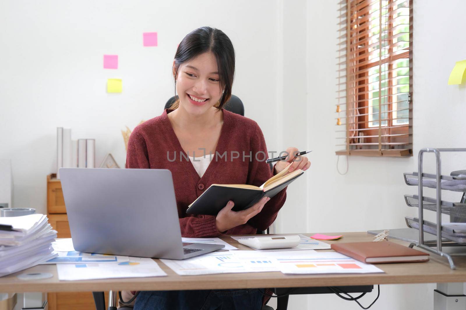 Portrait of an Asian young Female working on a laptop computer in home, Asian woman happy hold notebook and pen at home by wichayada