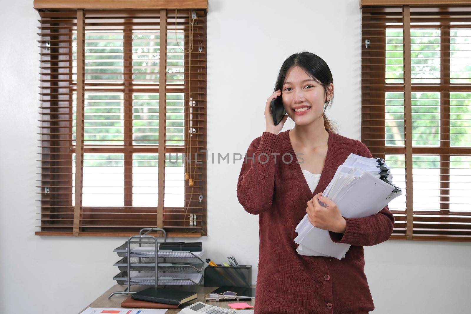 Asian businessman holding an accounting paper Financial Young Woman Spreadsheet Document Standing On The Phone Talking At Home Work Consulting.