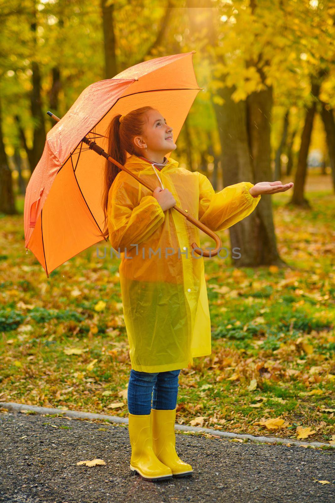 Happy child in the rain. Funny kid playing outdoors and catching rain drops in Autumn park