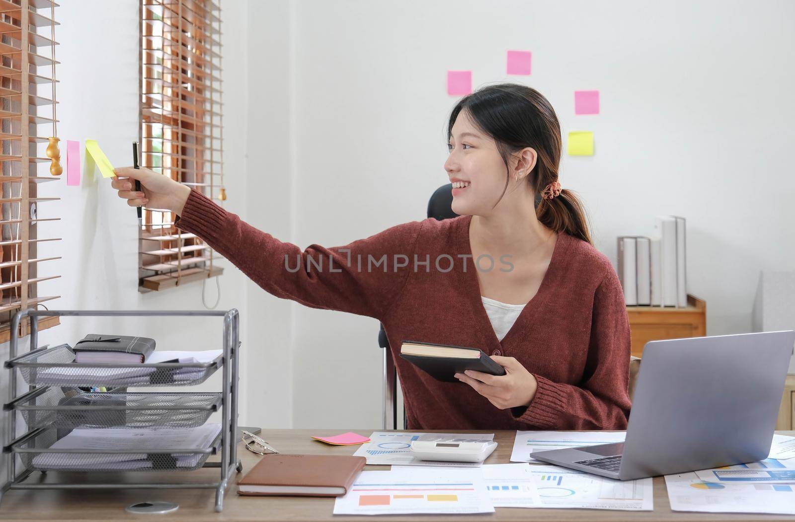 Business asian woman taking note on sticky note, Attractive girl working with laptop computer by wichayada