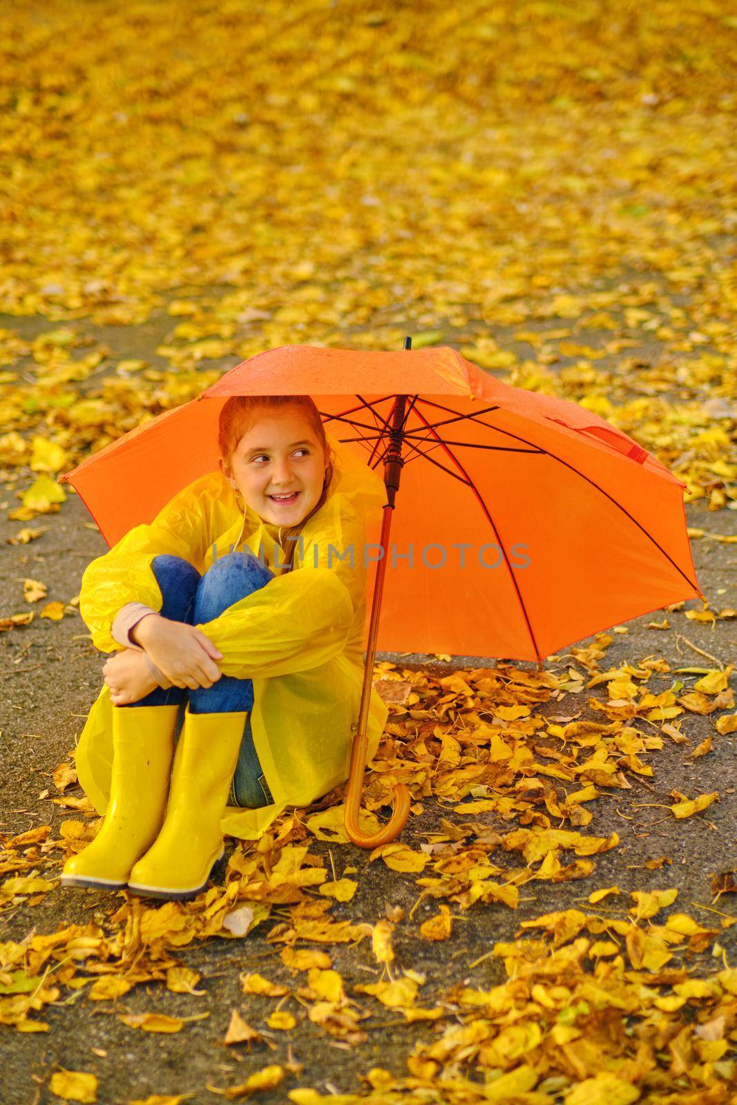 Happy kid Sits under an orange umbrella in the autumn park