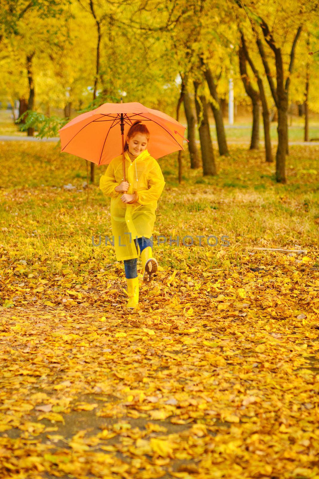 Happy child in the rain. Funny kid playing outdoors and having fun enjoying weather in autumn day in park