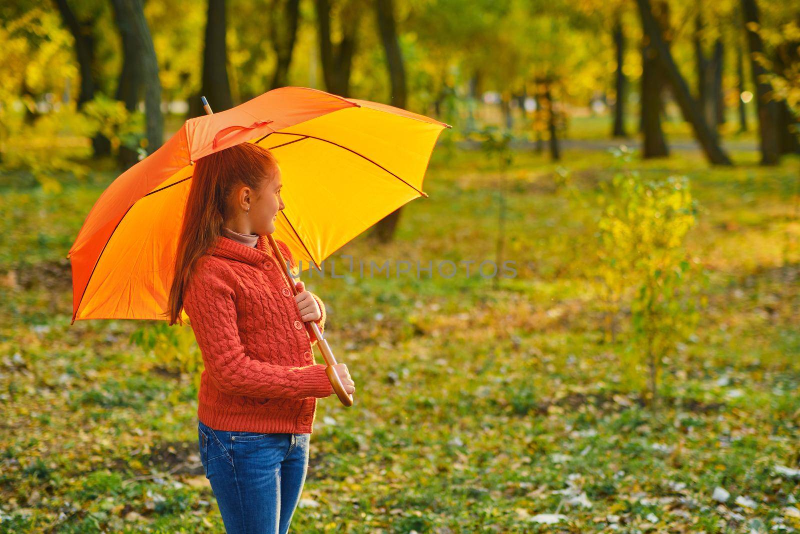 Funny kid under an orange umbrella outdoors in Autumn park