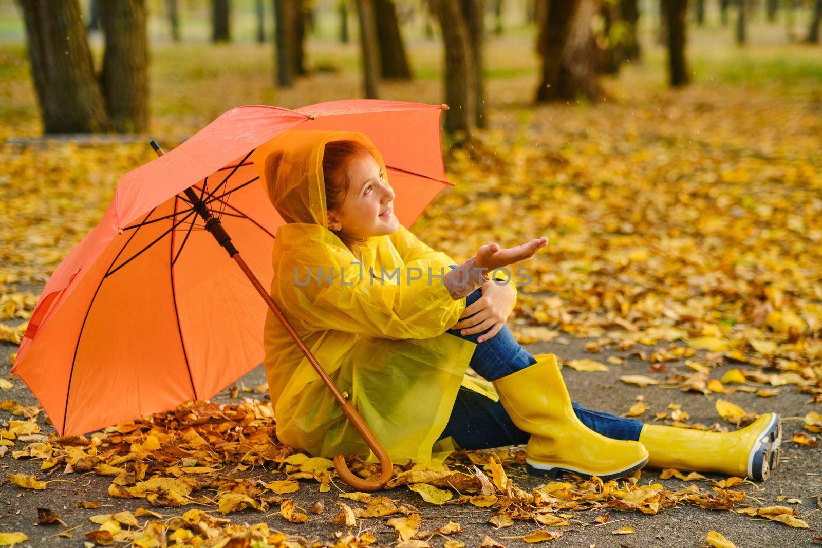 Happy kid Sits under an orange umbrella in the autumn park catching rain drops