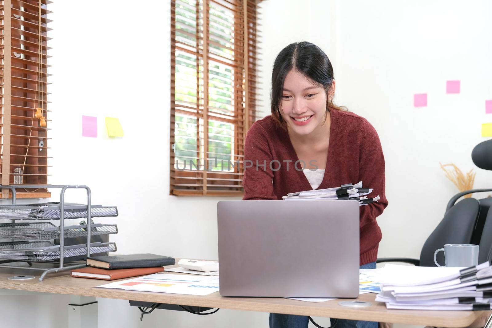 Asian businessman holding an accounting paper spreadsheet document Financial Advisory Job Standing Report on Laptop at Home by wichayada
