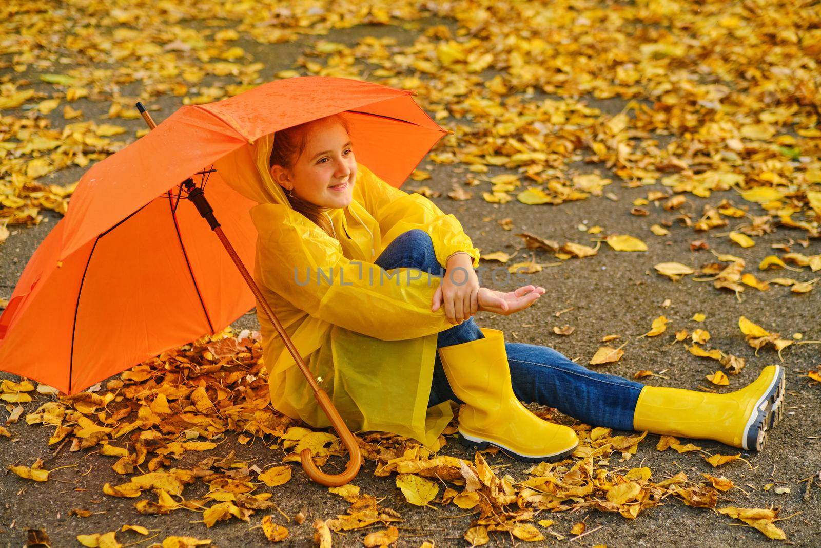 Happy kid Sits under an orange umbrella in the autumn park catching rain drops