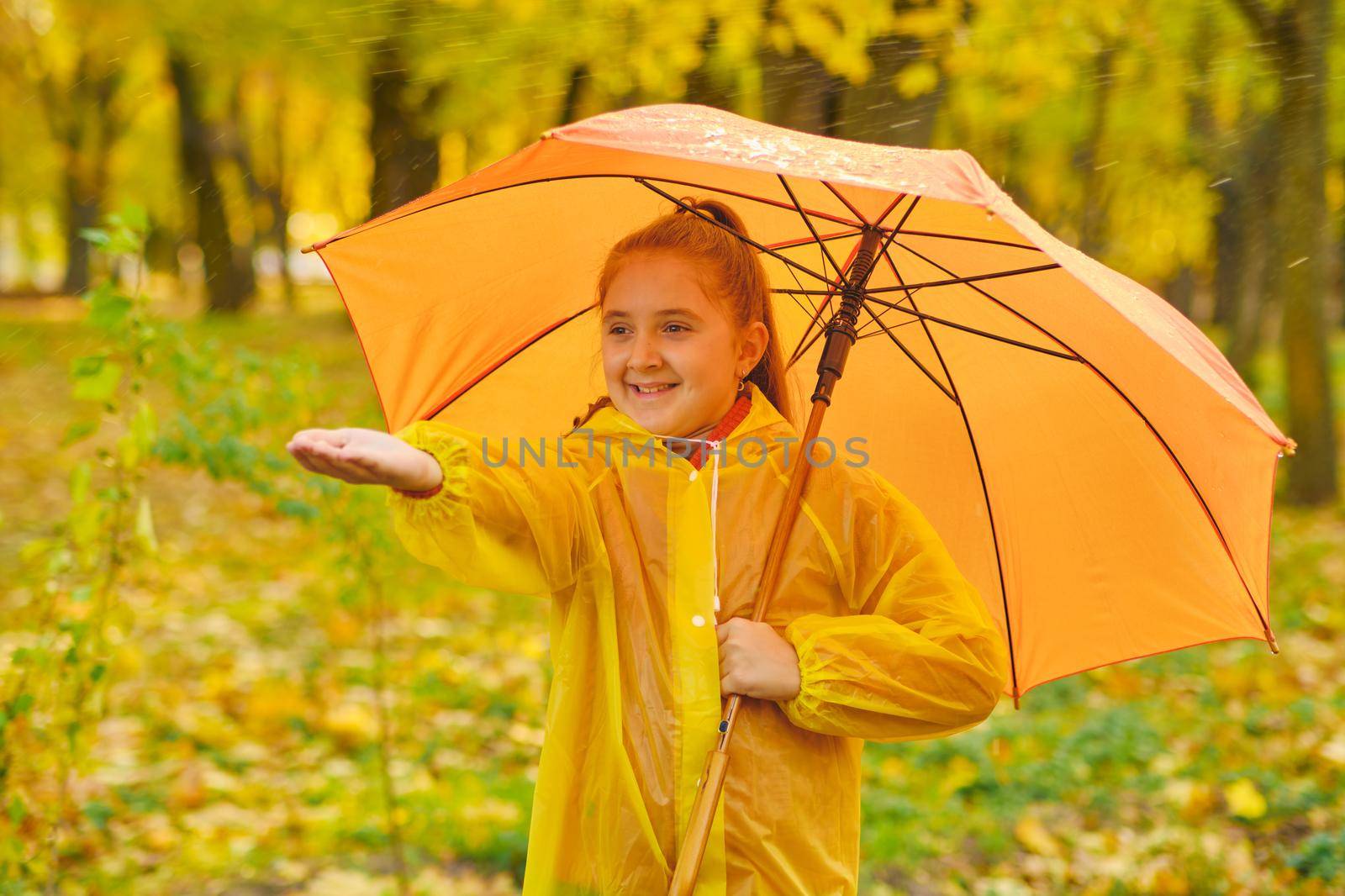 Happy child in the rain. Funny kid playing outdoors and catching rain drops in Autumn park