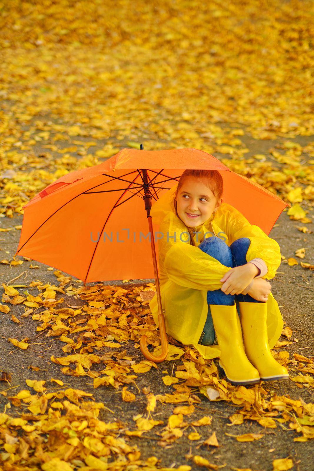 Happy kid Sits under an orange umbrella in the autumn park