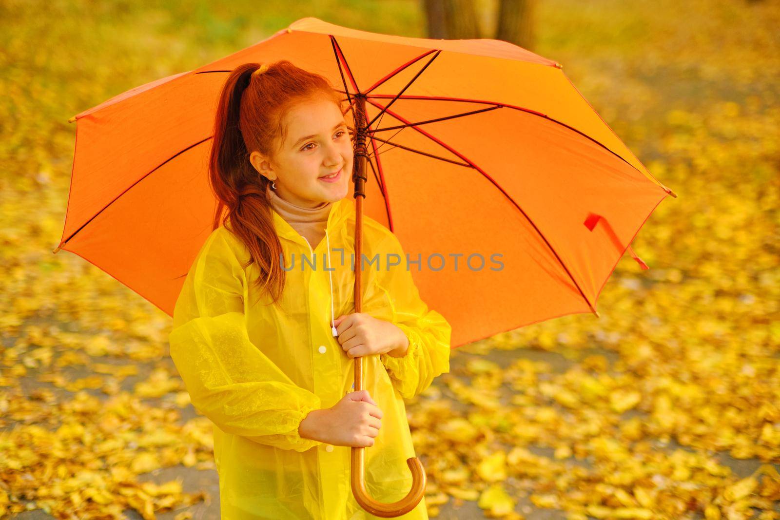 Happy child in the rain. Funny kid playing outdoors and catching rain drops in Autumn park