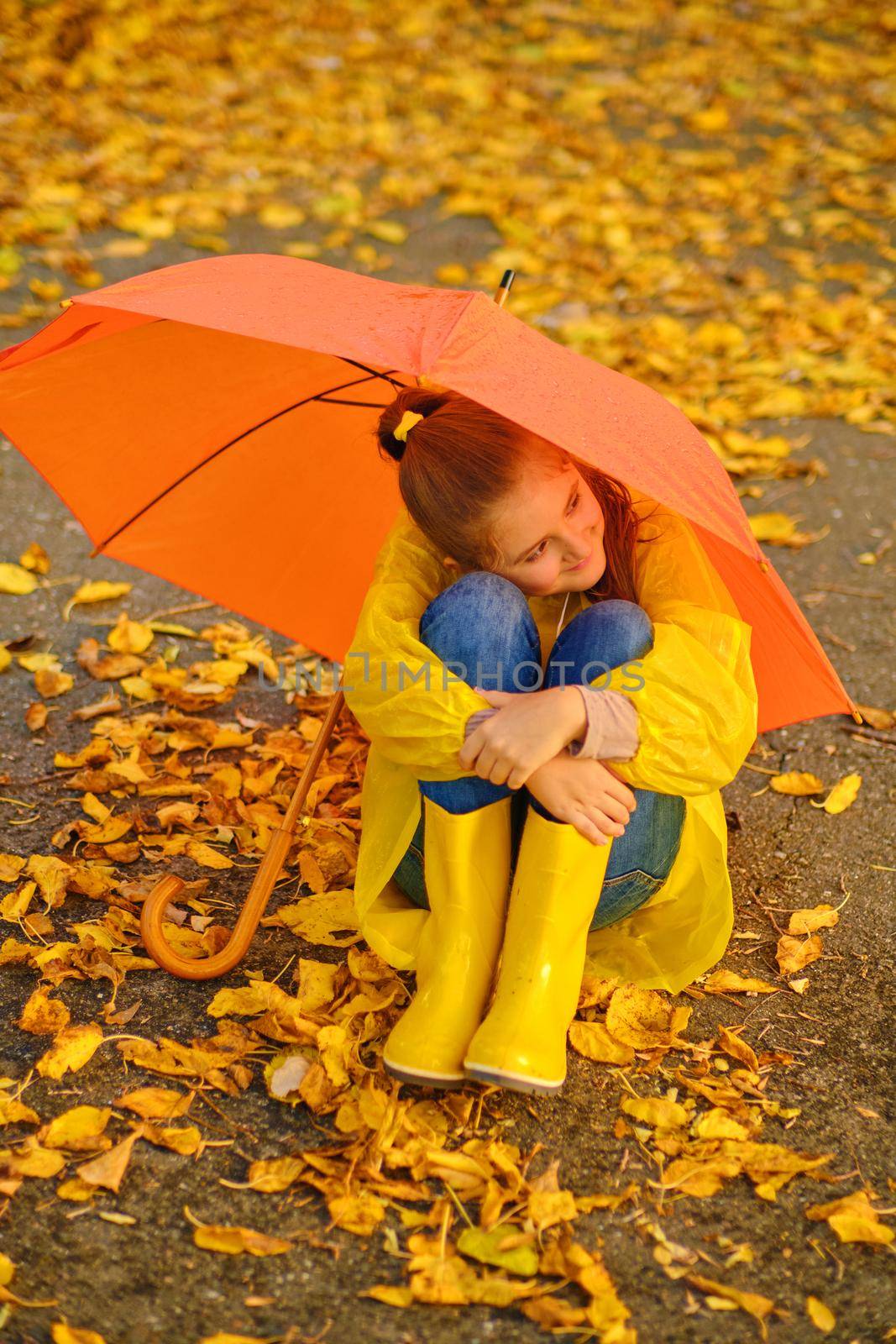 Happy kid Sits under an orange umbrella in the autumn park