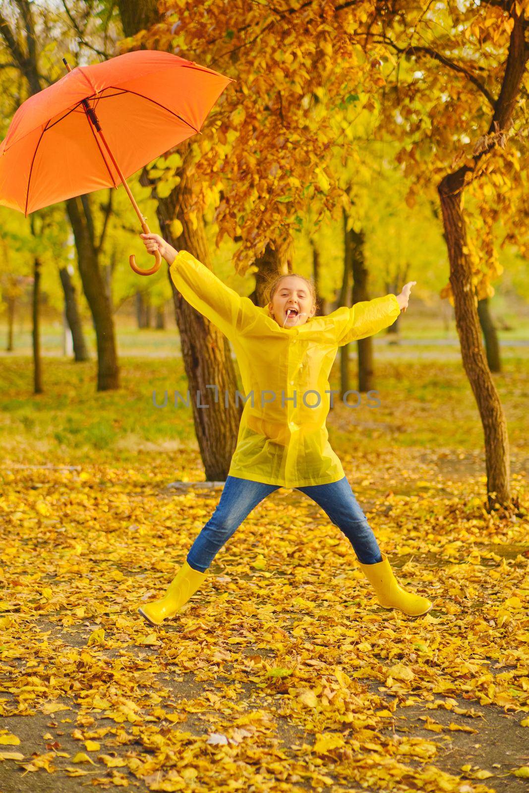 Happy child in the rain. Funny kid playing jumping and having fun enjoying weather in autumn day in park