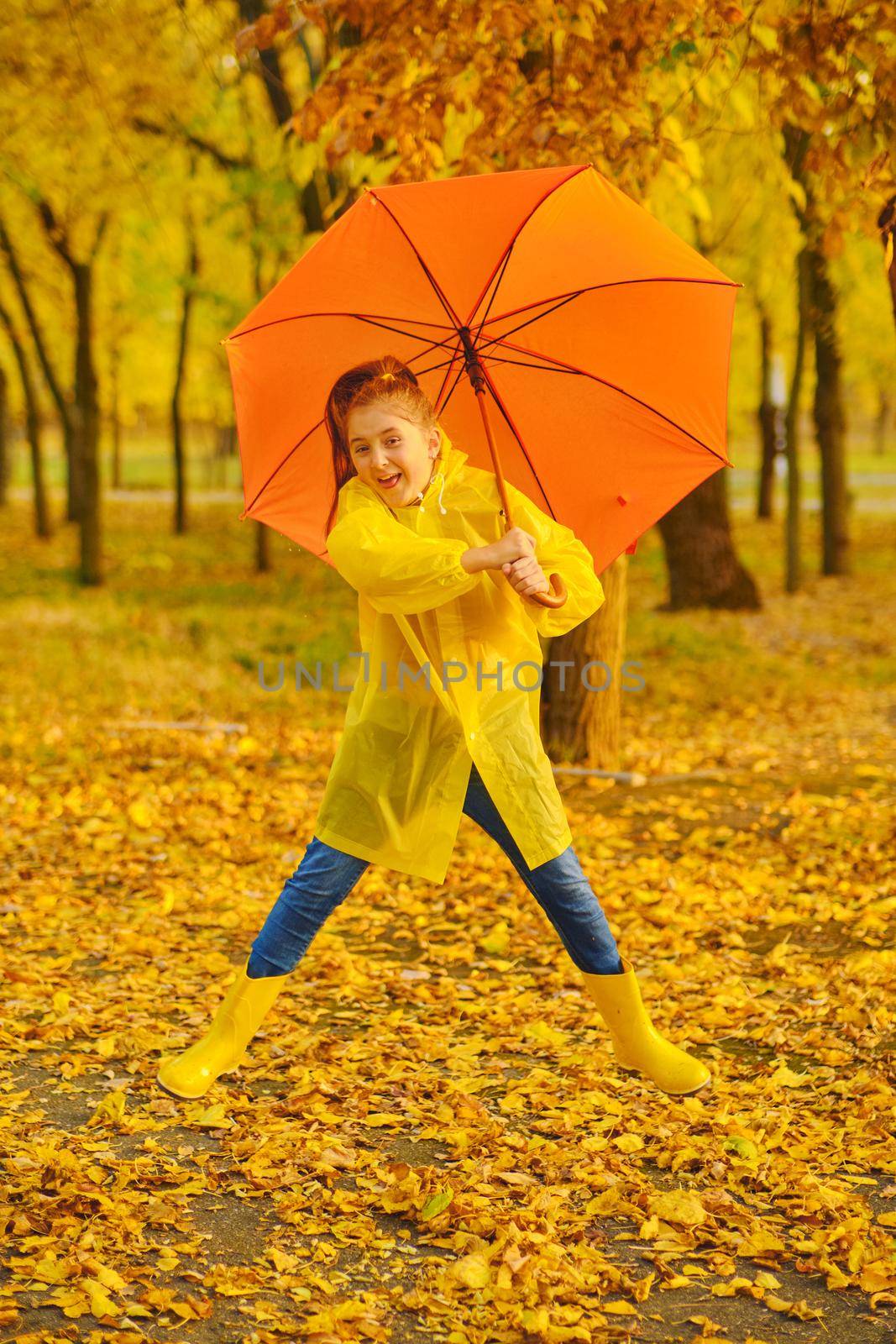 Happy child in the rain. Funny kid playing jumping and having fun enjoying weather in autumn day in park