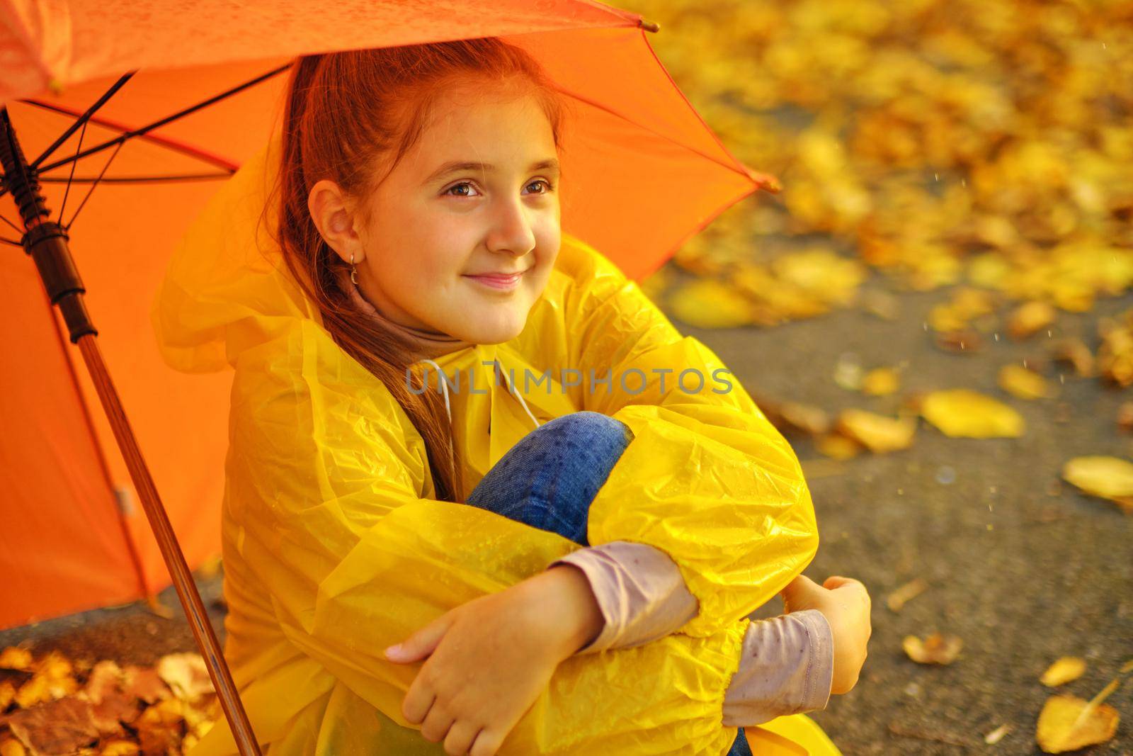 Happy kid Sits under an orange umbrella in the autumn park