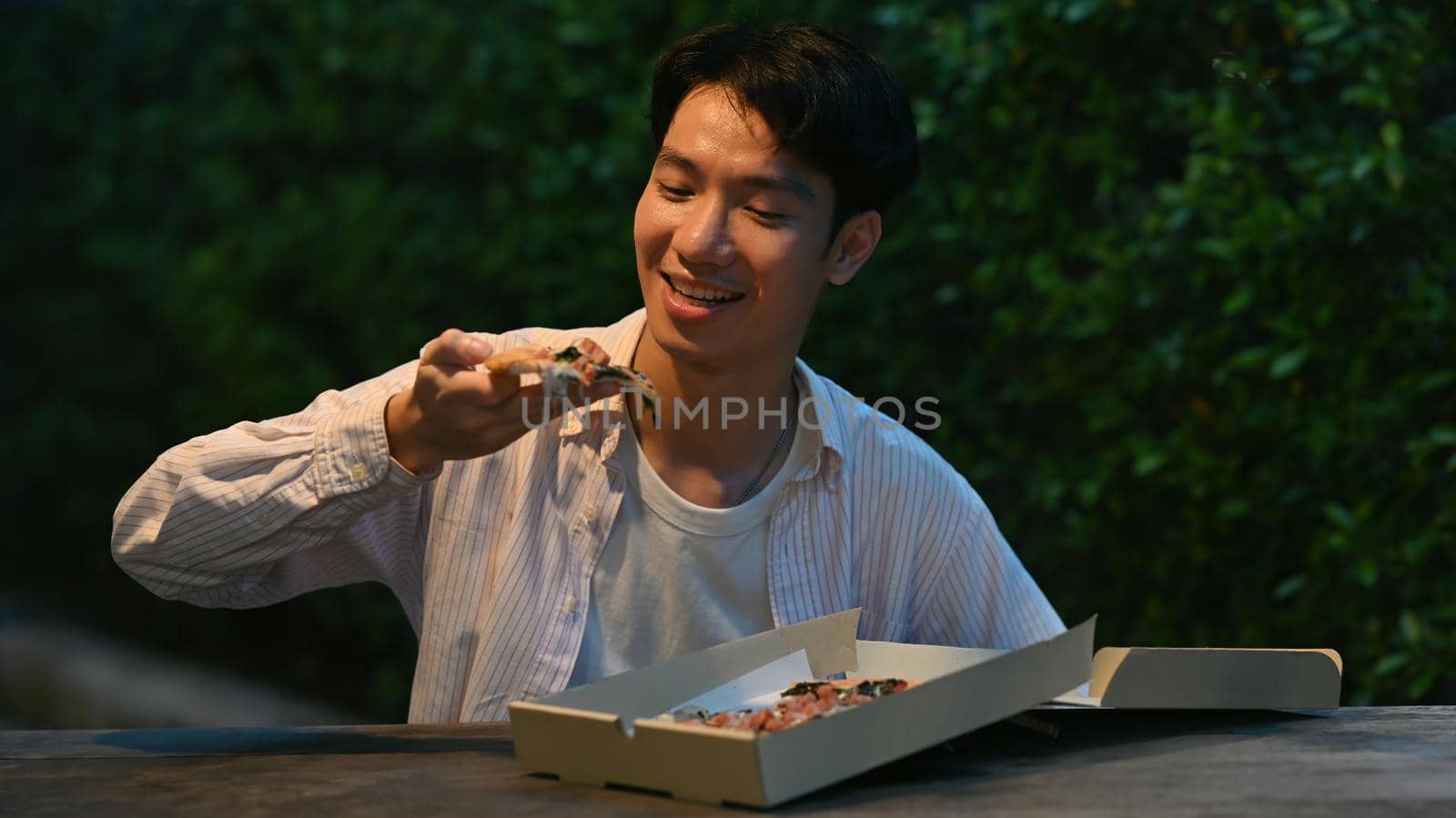 Happy young man eating eating pizza at outdoor at night market. Nightlife concept.