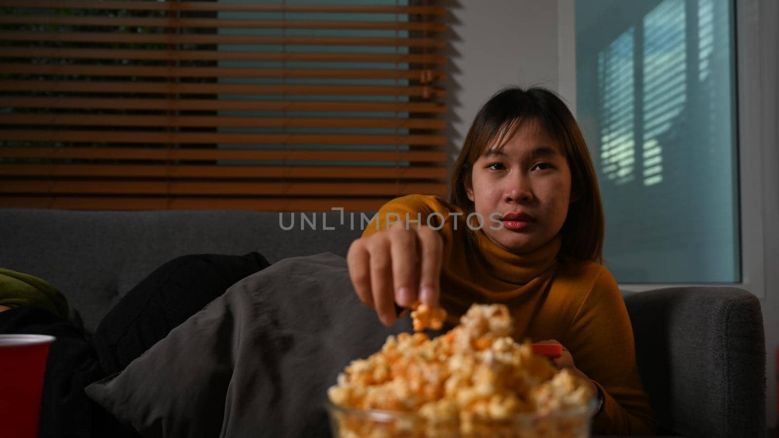 Young woman enjoy eating popcorn and watching movie on couch at home. Entertainment and leisure activity concept.