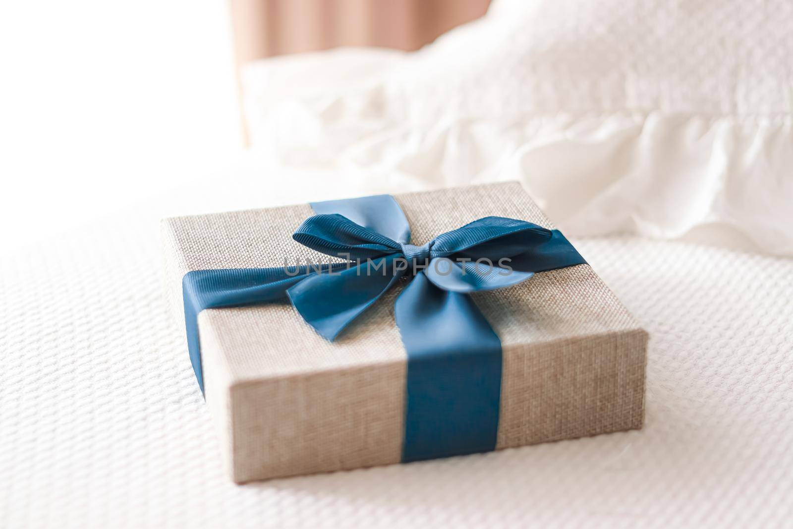 Holiday present and luxury online shopping delivery, wrapped linen gift box with blue ribbon on bed in bedroom, chic countryside style, close-up