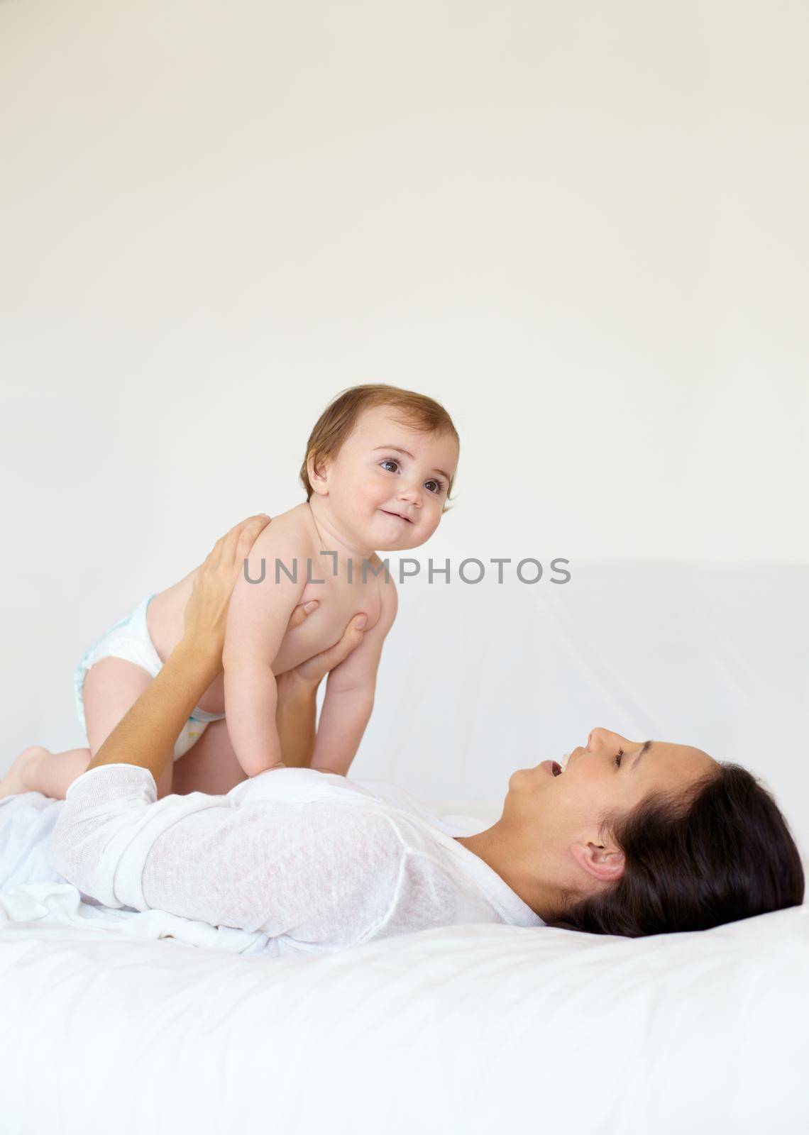Bonding with my baby. A young mother lying on her back and holding up her baby girl while laughing. by YuriArcurs