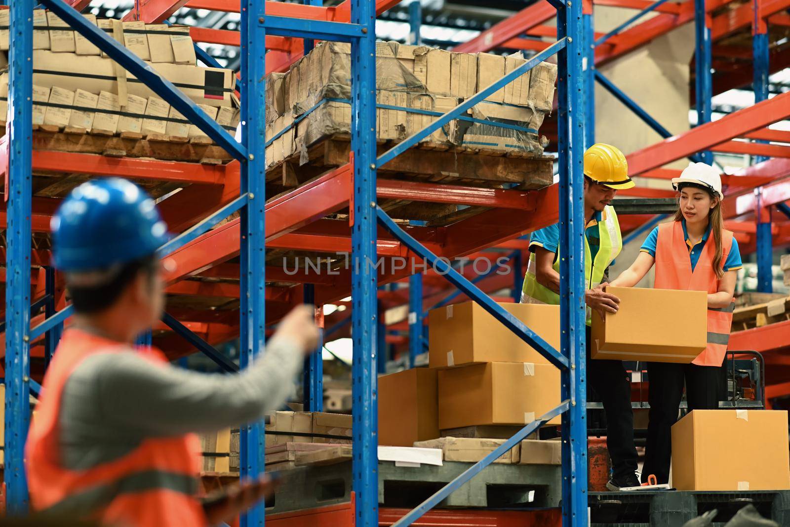 Warehouse workers wearing safety hardhat working on retail warehouse full of packed boxes and goods by prathanchorruangsak