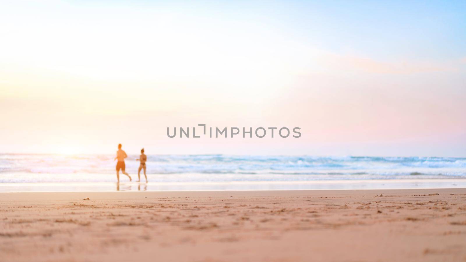 Couple running on the beach. Happy couple go to swim in ocean at sunset. Blurred summer vacation background. Defocused man and woman run on sandy sea beach. Summertime. Happy people